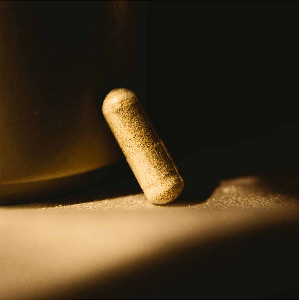 Macro image of a single beige supplement capsule resting on a surface in warm dramatic lighting.
